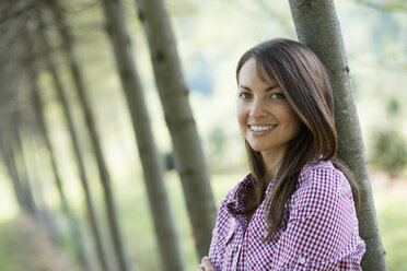 Eine Frau steht in einer Baumallee und lächelt. - MINF00349