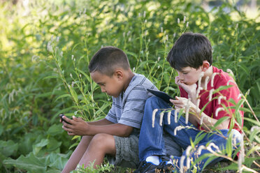 Zwei Jungen sitzen auf einem Feld, einer mit einem Smartphone, der andere mit einem digitalen Tablet. - MINF00353