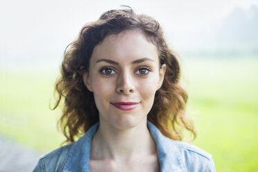 Eine junge Frau in einer ländlichen Landschaft, mit vom Wind verwehtem, gelocktem Haar, lächelnd. - MINF00379