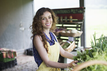 Ein Bio-Bauernhofstand: Eine Frau sortiert Gemüse. - MINF00387