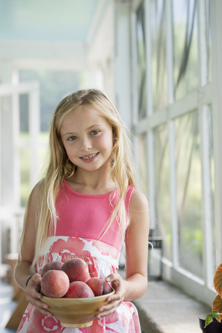 Ein junges Mädchen mit einem Arm voller frischer Pfirsiche., lizenzfreies Stockfoto