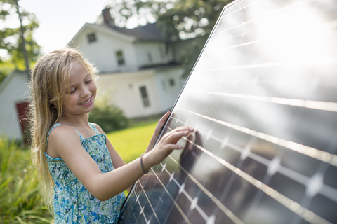 Ein junges Mädchen neben einem großen Solarmodul im Garten eines Bauernhauses., lizenzfreies Stockfoto