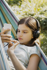 Porträt eines Mädchens mit Kopfhörern und Smartphone in der Hängematte - LVF07321