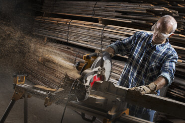 Ein Mann mit Schutzbrille arbeitet mit einer Kreissäge, um Holz zu schneiden. - MINF00412
