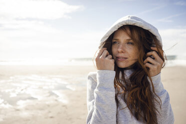 Netherlands, Zeeland, portrait of redheaded woman wearing hooded jacket on the beach - KNSF04195