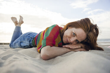 Niederlande, Zeeland, Porträt einer lächelnden Frau, die im Sand am Strand liegt - KNSF04204