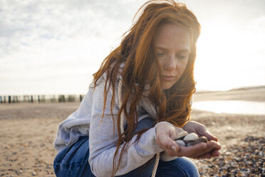 Niederlande, Zeeland, Porträt einer rothaarigen Frau mit gesammelten Muscheln am Strand - KNSF04206