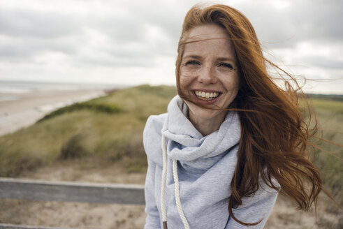 Netherlands, Zeeland, portrait of happy redheaded woman on the beach - KNSF04208