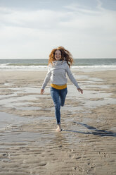 Netherlands, Zeeland, happy redheaded woman running on the beach - KNSF04209