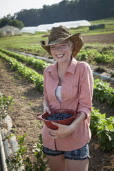 A girl in a pink shirt holding a large bowl of harvested blueberry fruits. - MINF00453