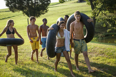 Eine Gruppe junger Leute, Jungen und Mädchen, mit Handtüchern und Schwimmflügeln in der Hand, geht schwimmen. - MINF00457