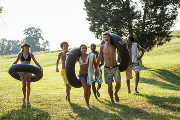 Eine Gruppe junger Leute, Jungen und Mädchen, mit Handtüchern und Schwimmflügeln in der Hand, geht schwimmen. - MINF00458