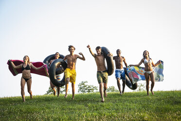 A group of teenagers, boys and girls, running across the grass holding swim towels and inflated floats. - MINF00461
