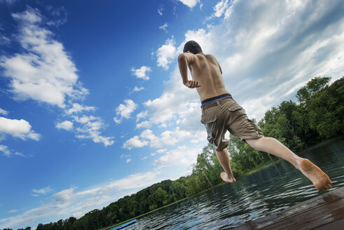 A boy taking a running jump into a calm pool of water, from a wooden jetty. - MINF00465