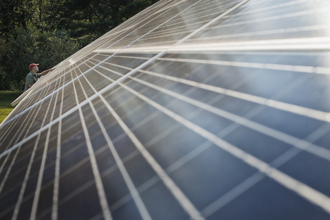 Ein Mann inspiziert die Oberfläche einer großen, geneigten Solarpanelanlage zur Nutzung der Sonnenenergie., lizenzfreies Stockfoto