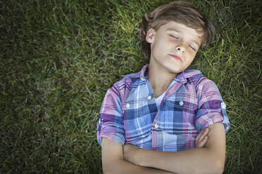 A boy with arms folded lying on the grass, eyes closed. - MINF00479