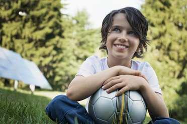 Ein Junge mit einem Fußball in der Hand, der im Gras sitzt. Solarzellen. - MINF00492