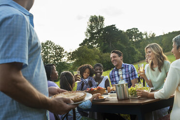 Eine Familie und Freunde sitzen an einem Tisch im Freien und essen. - MINF00507