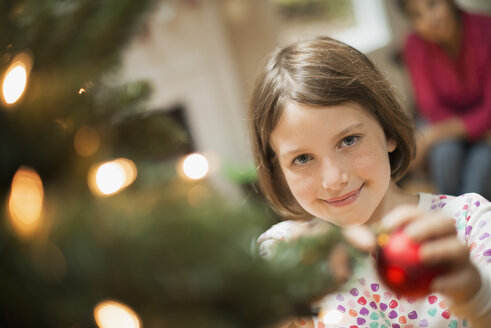 Ein Mädchen, das ein handgefertigtes Ornament an einen Weihnachtsbaum hängt. - MINF00512