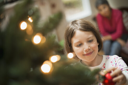 Ein Mädchen, das ein handgefertigtes Ornament an einen Weihnachtsbaum hängt. - MINF00513