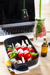 Lunchpaket mit Caprese-Salat, einer Flasche Mineralwasser und einem Laptop auf dem Schreibtisch - SBDF03672