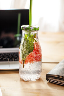 Glasflasche mit Entgiftungswasser mit roter Grapefruit und Minze auf dem Schreibtisch - SBDF03673