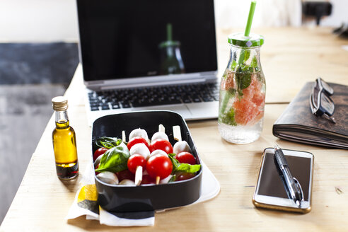 Lunch box of Caprese salad, bottle of infused water and laptop on desk - SBDF03674