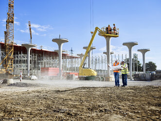 Arbeiter auf der Baustelle, die zusammen mit dem Architekten einen Bauplan betrachten - CVF00972