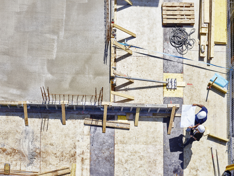 Arbeiter und Architekt betrachten einen Bauplan auf einer Baustelle, lizenzfreies Stockfoto