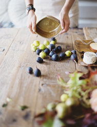 Eine Frau am heimischen Küchentisch, die frisches Obst, schwarze und grüne Feigen auf einer Käseplatte arrangiert. Bio-Lebensmittel. Vom Bauernhof auf den Teller. - MINF00566