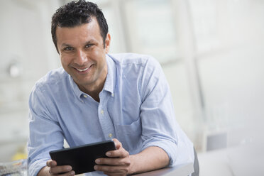Ein Mann in einem blauen Hemd lehnt an einem Schreibtisch und hält ein digitales Tablet. - MINF00569