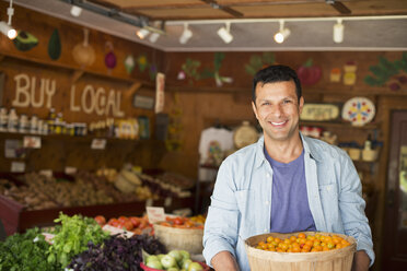 A farm growing and selling organic vegetables and fruit. A man holding a bowl of basket of freshly picked tomatoes. - MINF00586