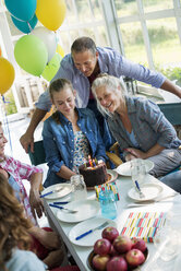 Eine Geburtstagsfeier in der Küche eines Bauernhauses: Eine Gruppe von Erwachsenen und Kindern versammelt sich um einen Schokoladenkuchen. - MINF00603