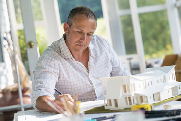 A farmhouse kitchen. A model of a house on the table. Designing a house. A man using a pencil drawing on a plan. - MINF00609