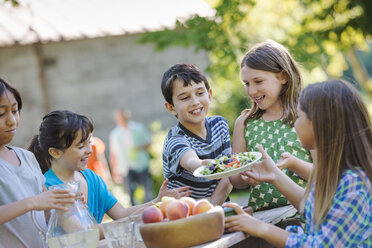 Eine Gruppe von Kindern sitzt an einem Tisch und isst frisches Obst und Salat. - MINF00639