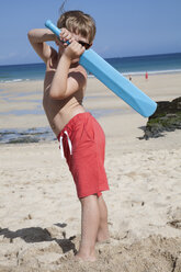 A boy standing on the sand with a small blue cricket bat in his hands. - MINF00650