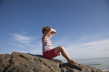 A child seated on the rocks looking out to sea. - MINF00651