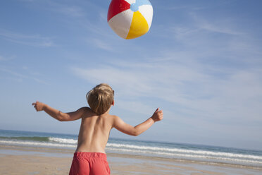 A boy in swimming trunks on the beach, with a large beach ball in the air above him. - MINF00652