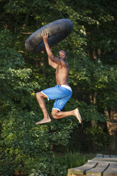 A young person, boy holding a swim float tyre over his head and leaping into the water from the jetty. - MINF00676