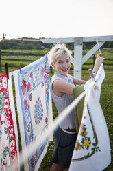 A young girl, teenager, hanging out the washing, pegging patterns fabric sheets to a washing line. - MINF00677