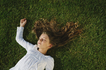 Neunjähriges Mädchen lächelt und ruht sich auf einem Feld mit saftigem, grünem Gras aus - MINF00713