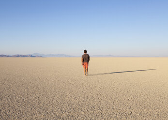 Man walking across a flat desert landscape - MINF00725