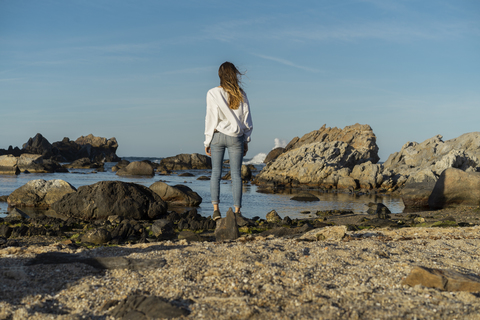 Frau auf Felsen sitzend, mit Blick auf das Meer, lizenzfreies Stockfoto