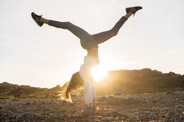 Young woman at the beach, doing handstand at sunset - AFVF00886