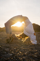 Junge Frau am Strand, die bei Sonnenuntergang eine Rad-Pose einnimmt - AFVF00888