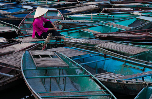 Lost in thought, a woman sits amidst a raft of boats. Ninh Binh, Vietnam - MINF00905