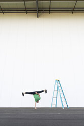 Acrobat training one-armed handstand next to ladder - AFVF00894