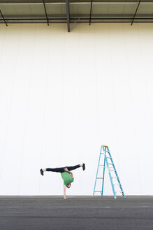 Acrobat training one-armed handstand next to ladder - AFVF00894