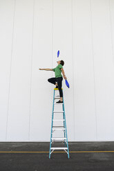 Acrobat standing on ladder, juggling - AFVF00914