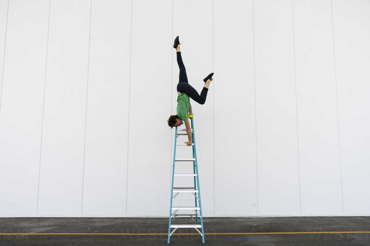 Acrobat balancing upside down on a ladder stock photo